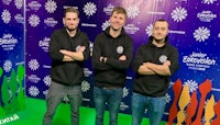 three men in black hoodies standing in front of a green screen