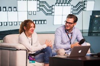 a man and woman sitting on a couch talking on a laptop